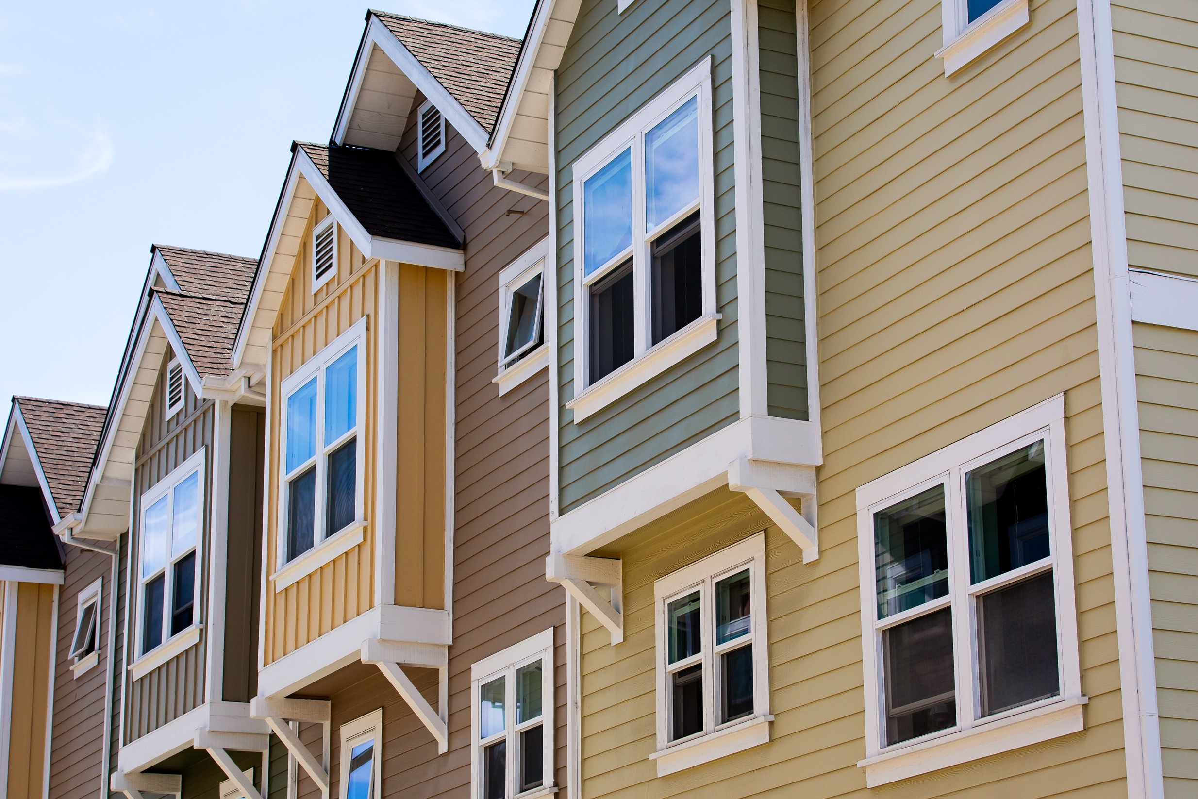 Row of modern townhomes in Columbia, MD under bright sunlight, illustrating heat buildup and need for attic fan installation.